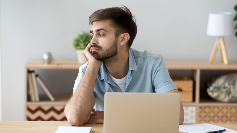 Hombre en oficina con cara de aburrimiento y con la cara apoyada en la mano. Es la portada de nuestro recurso gratuito La motivación bien intencionada en la empresa. Cómo evitarla